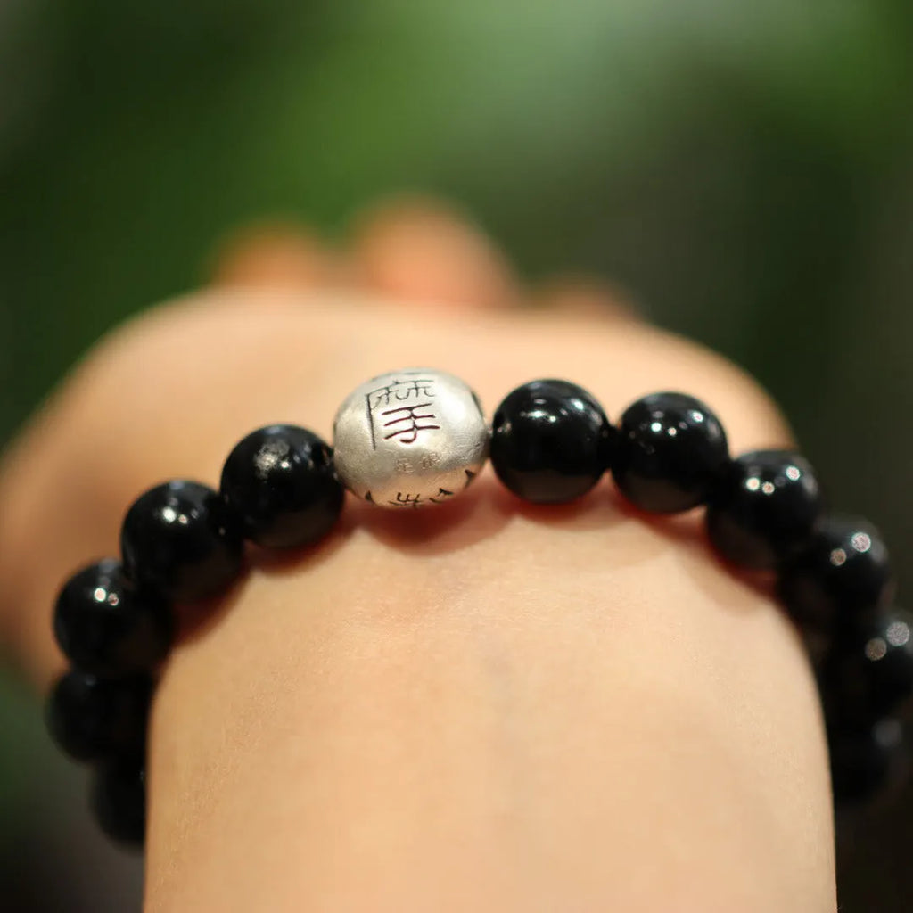 Close-up of a black bracelet with 10mm agate beads and sterling silver details on a wrist.