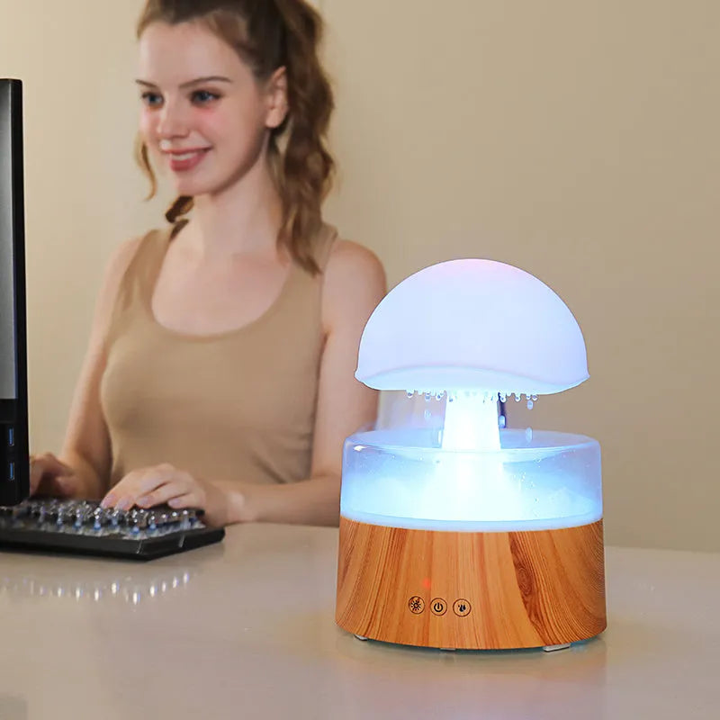 White plastic rain cloud humidifier with mist and coloured night light on a wooden surface