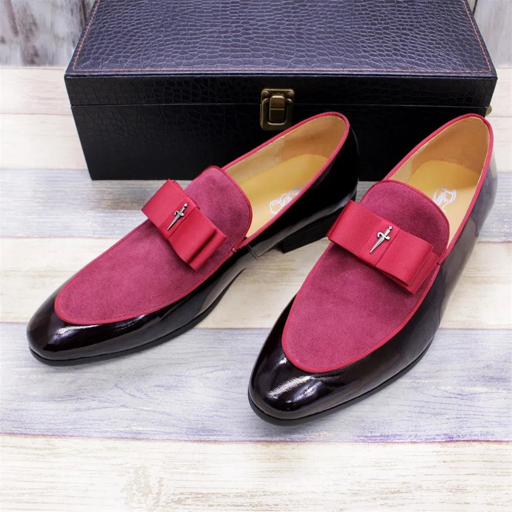 Men's glossy black patent leather tassel loafers with a low-top design and rubber sole on a wooden floor.