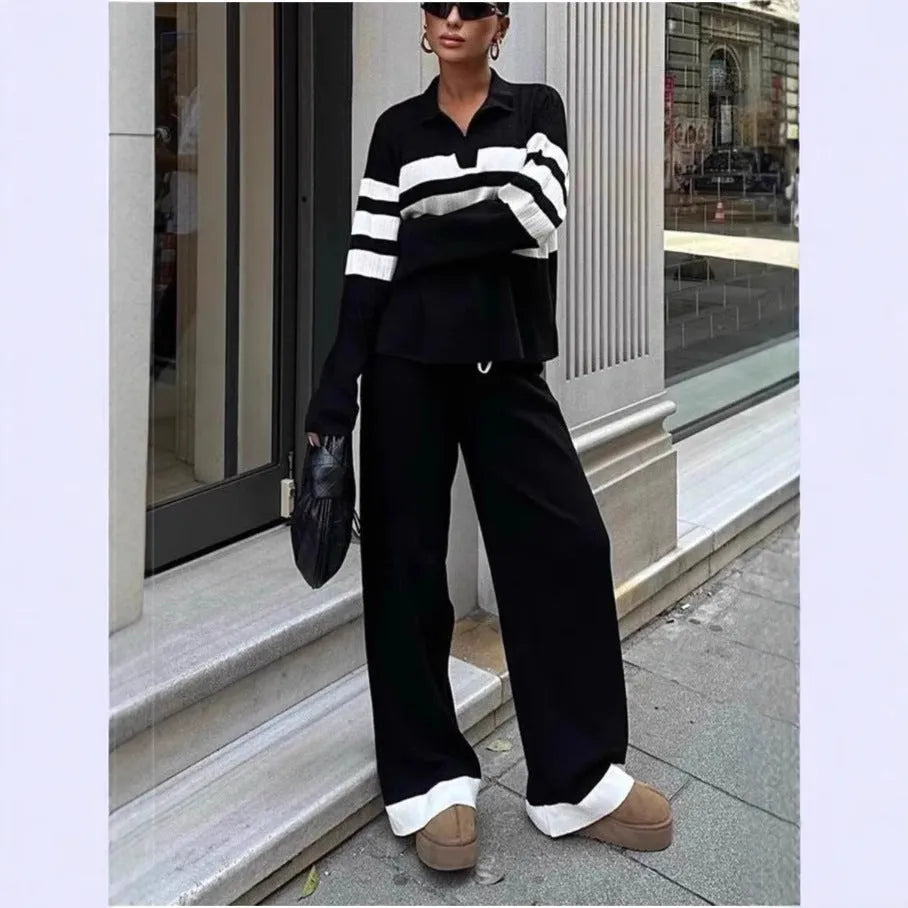 Women's black knitted polo shirt with white stripes and matching trousers laid flat.
