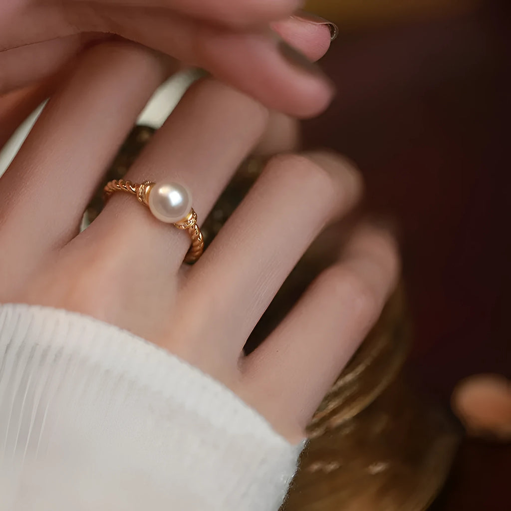 Close-up photo of an antique-style twisted copper ring with a small white pearl inlaid on a person's finger.