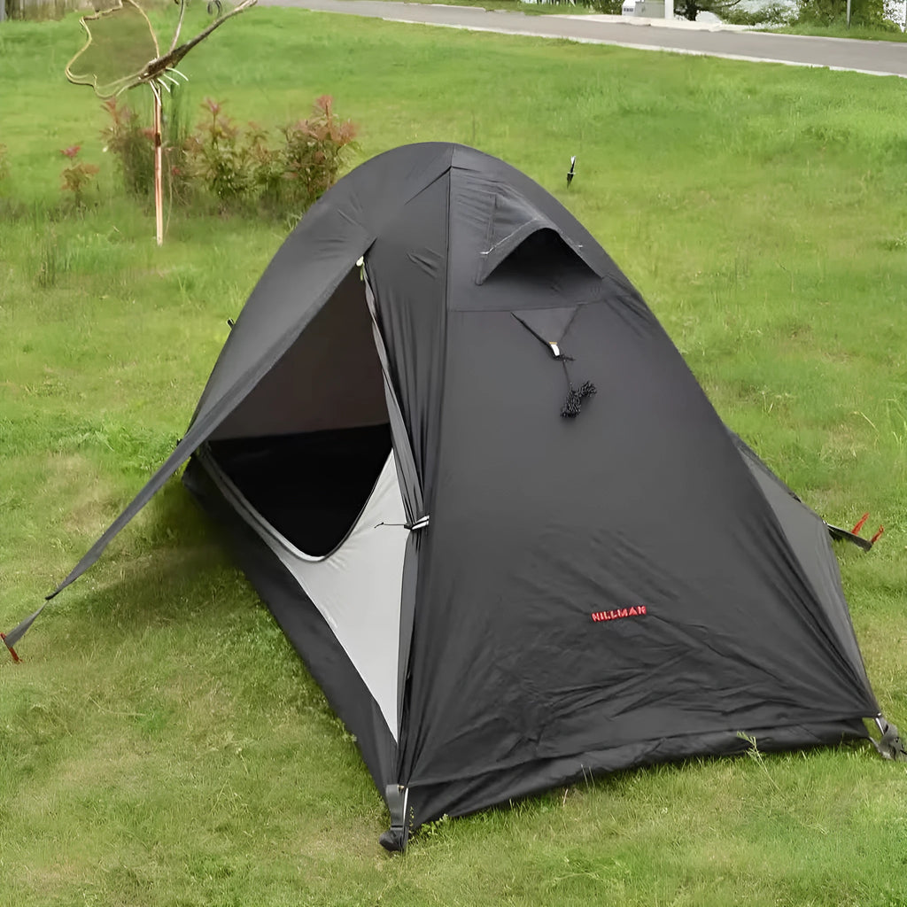 Single person hiking tent in orange pitched in a forest, showing aluminium poles and double-layer design with mesh panel.
