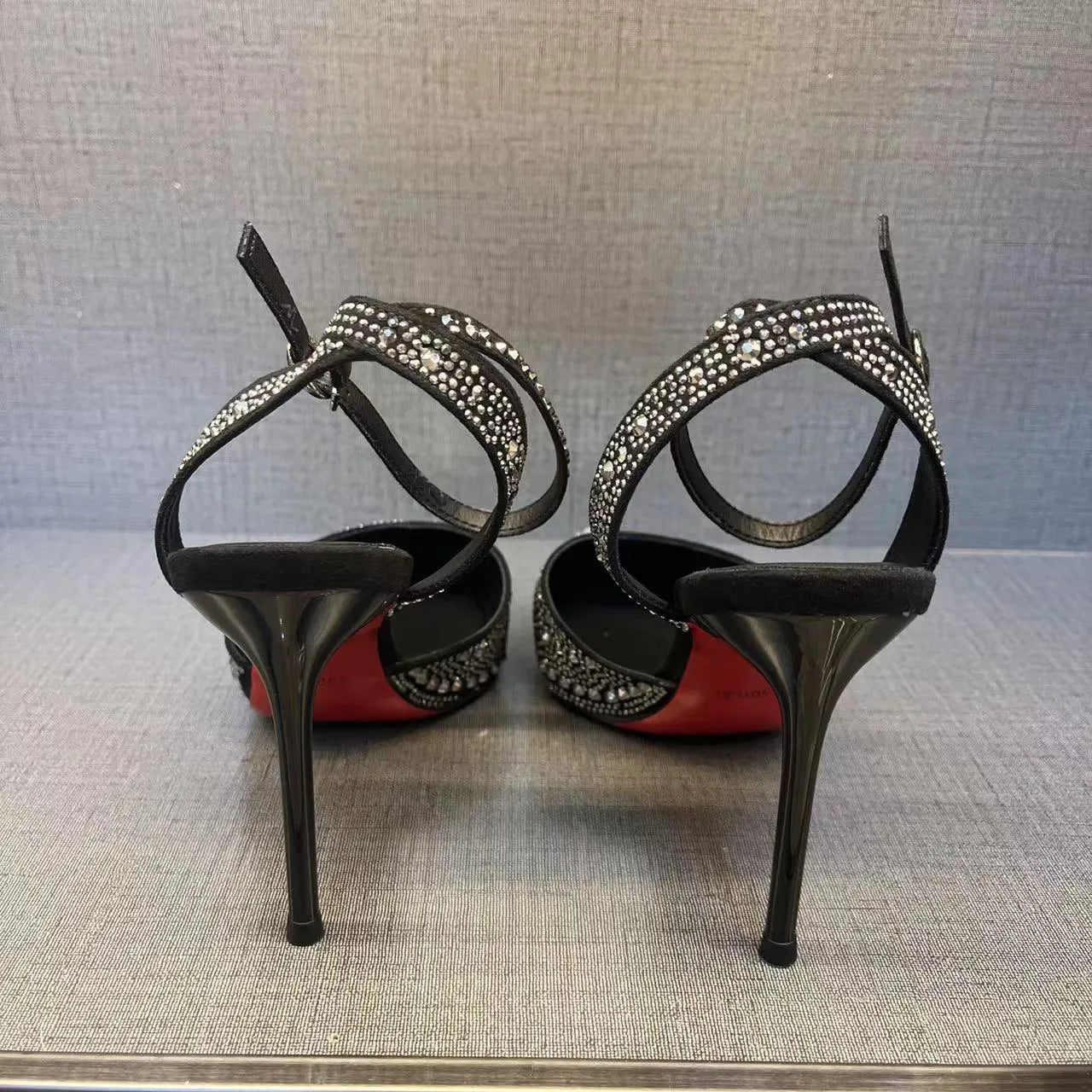 Women's black hollow high heel shoe with red sole and pointed toe, shown next to a silver pair.