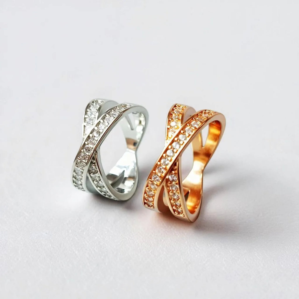 A silver or rose gold plated metal ring with a cross design and small zircon stones, shown on a finger.