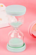A glass hourglass sand timer on a desk, showing purple sand flowing between bulbs.