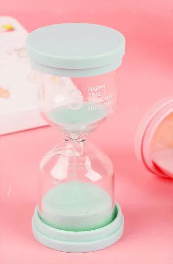 A glass hourglass sand timer on a desk, showing purple sand flowing between bulbs.