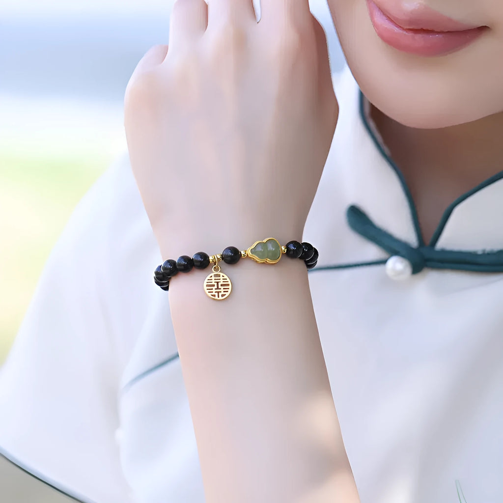 Black obsidian bracelet with a carved Hetian jade gourd charm, showing geometric beads.