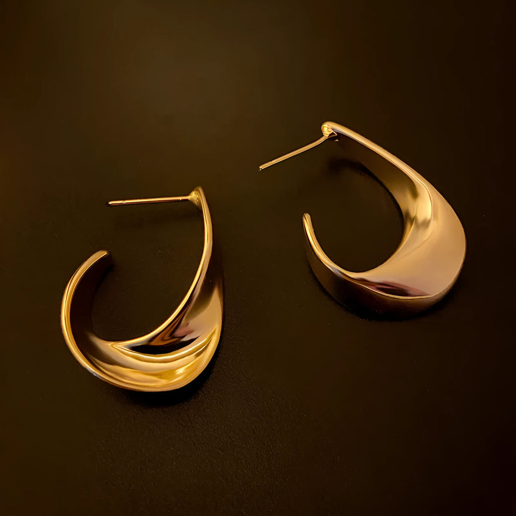 A pair of twisted geometric round metal earrings with a gold electroplated finish on a white background.