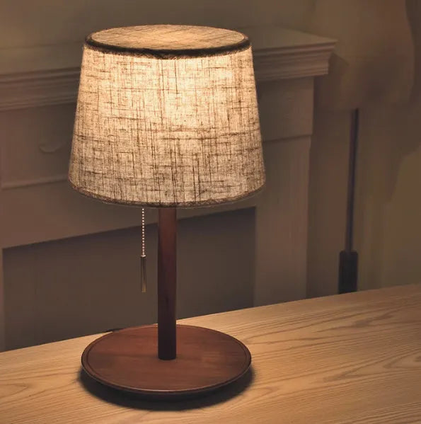 Walnut coloured solid wood bedside lamp with a white cloth lampshade and a black cable switch.