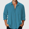 Man wearing a loose-fit blue casual shirt with a stand collar and long sleeves on a beach.