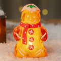 Glowing plastic gingerbread man and snowman Christmas ornament with a red scarf on a festive background.