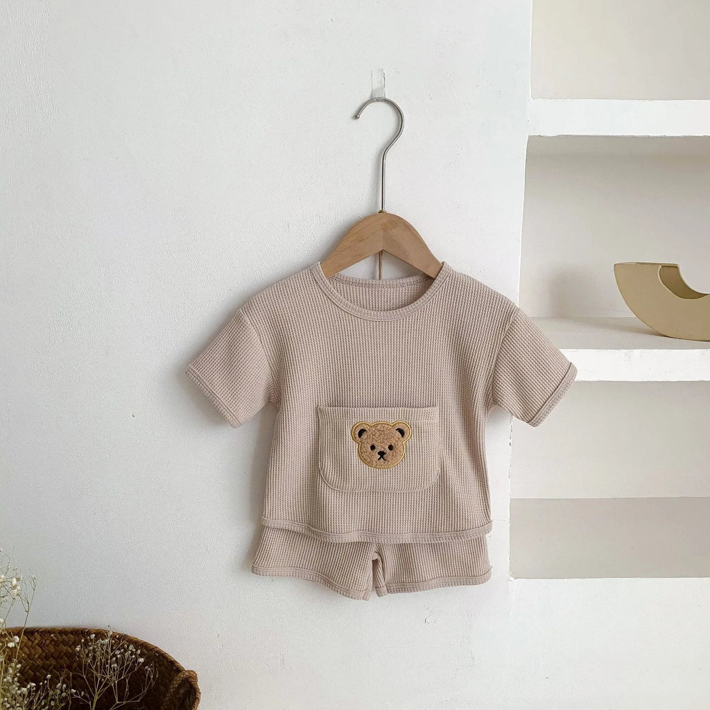Unisex baby summer suit with bear print cotton top and beige shorts on a neutral background