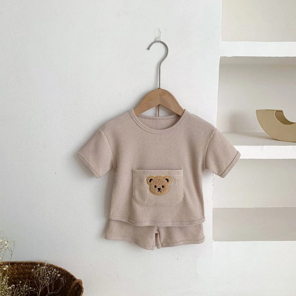 Unisex baby summer suit with bear print cotton top and beige shorts on a neutral background