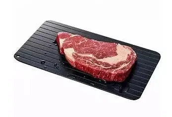 Black aluminium fast defrosting tray with silica gel feet on a kitchen countertop.