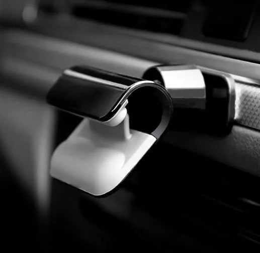 Black universal car phone holder with 360-degree rotating head mounted on a car air vent, holding a mobile phone.