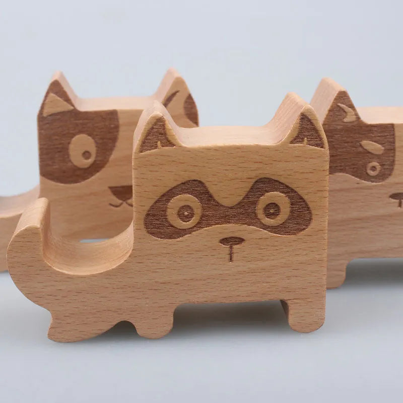 Solid beech wood phone stand with a decorative resin puppy figurine, holding a mobile phone at an angle with a charging cable threaded through the back.