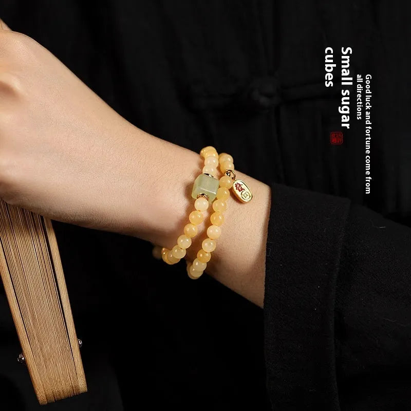 Close-up of a women's hand-woven bracelet with topaz-coloured barrel beads, square jade beads, and a fu charm.
