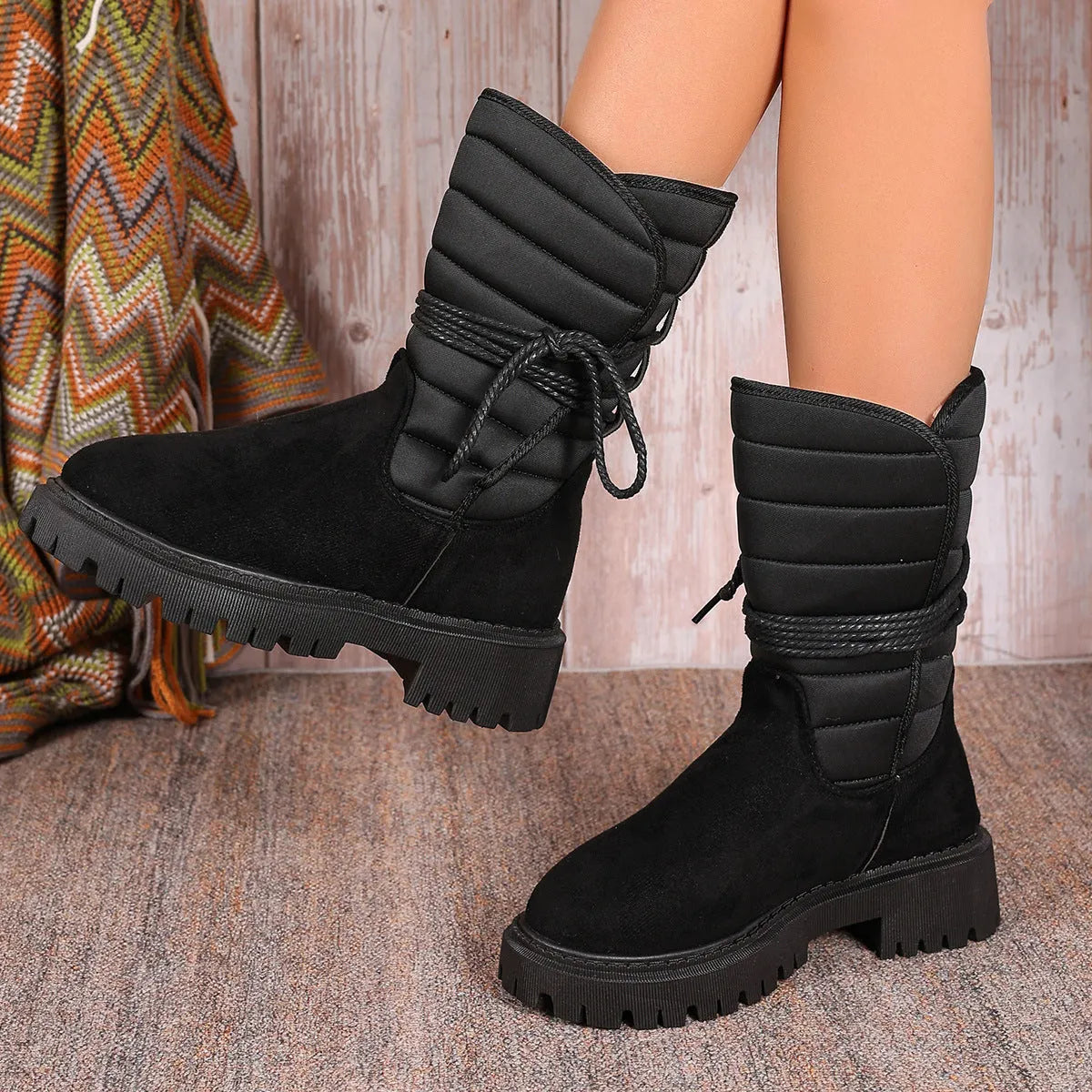 A pair of women's chunky heel snow boots in suede with a lace-up front and fleece lining, shown in black.
