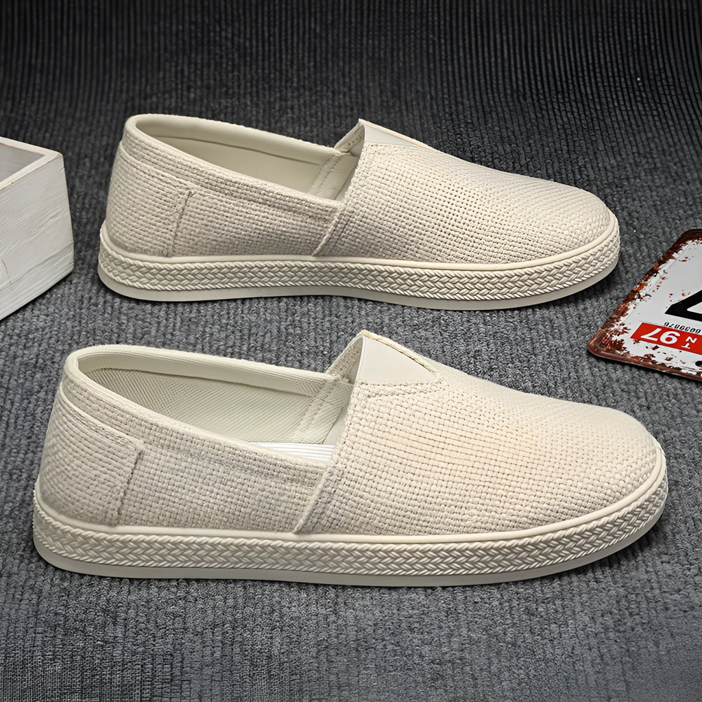 Men's beige linen canvas slip-on shoes with round toe and shallow cut design on a grey background.