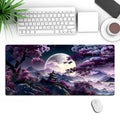 Large black gaming desk mat with stitched edges shown on a desk with keyboard and mouse.