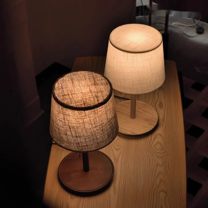 Walnut coloured solid wood bedside lamp with a white cloth lampshade and a black cable switch.