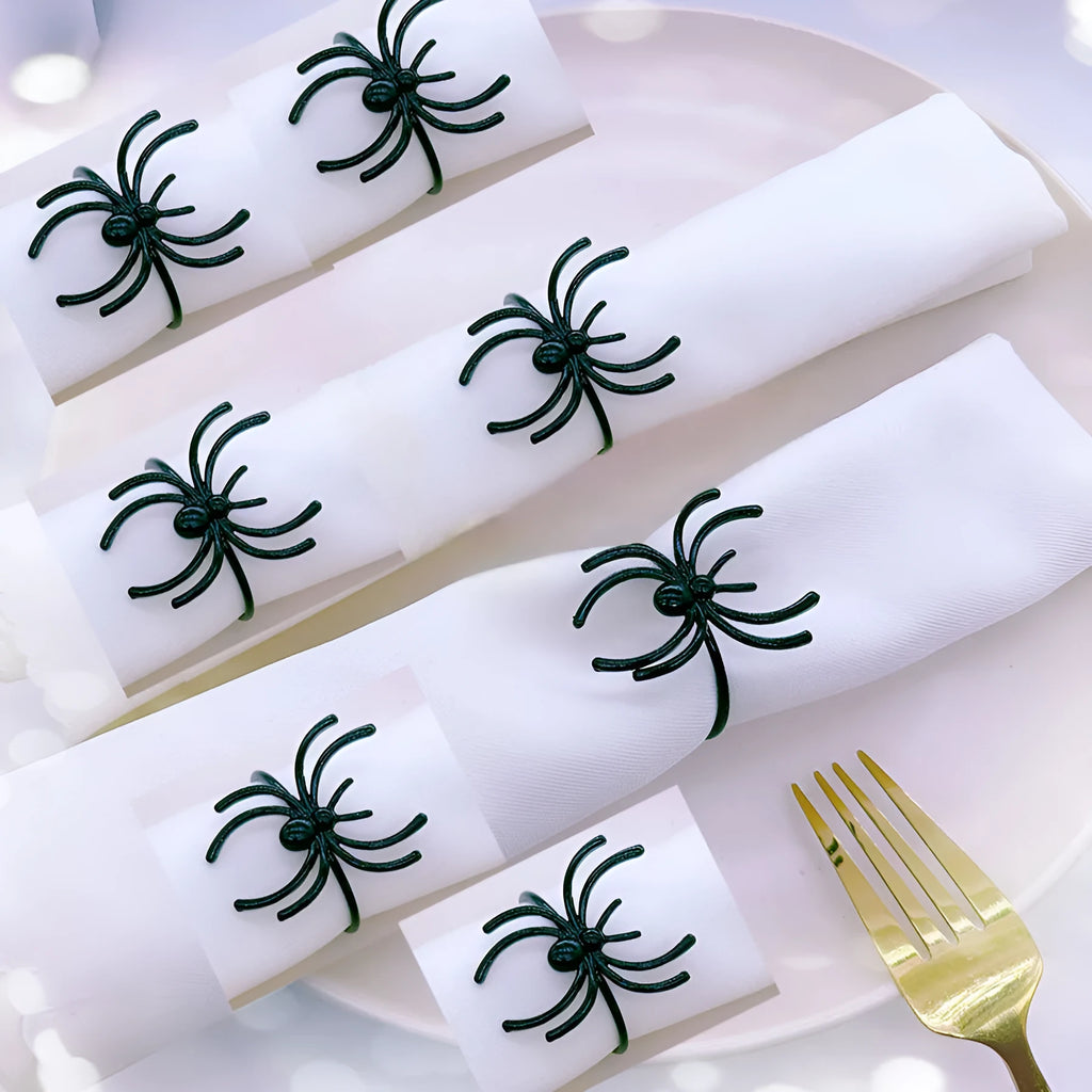 Set of six black alloy spider-shaped napkin rings on a dark tablecloth.