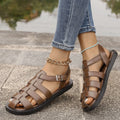 Flat Roman style women's sandals with buckle, black PU upper and rubber sole, side view