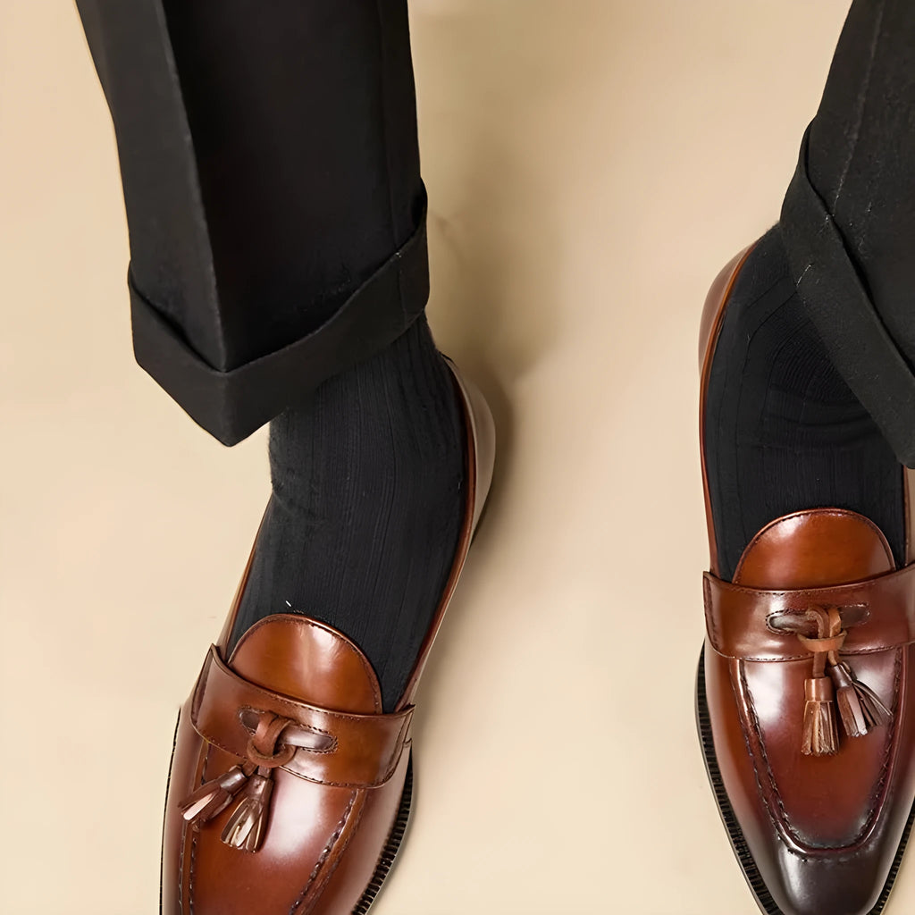 Men's black polished leather tassel loafers with rubber sole, shown from the side.