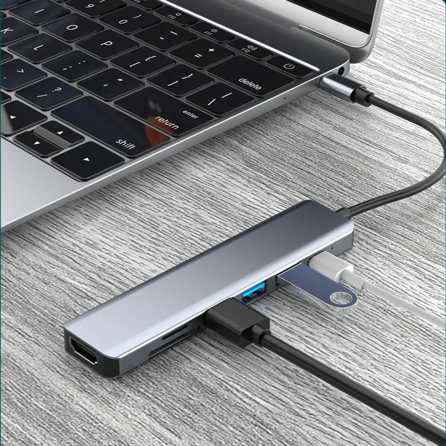 Silver 7-in-1 USB C hub docking station with HDMI, USB ports, and card readers on a desk.