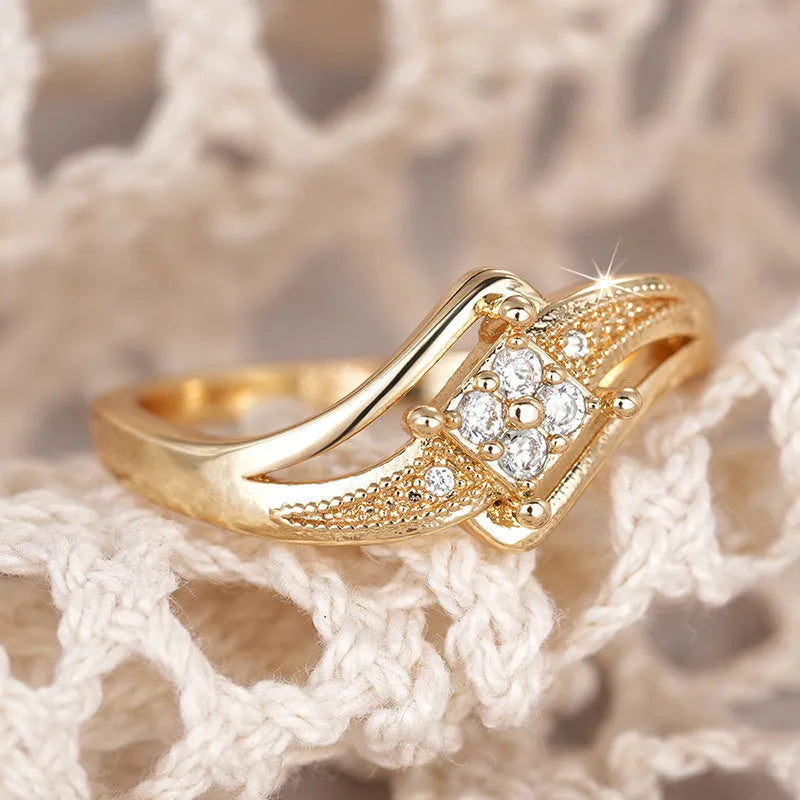 Yellow gold women's geometric diamond ring with a small inlaid zircon stone, shown on a copper band.