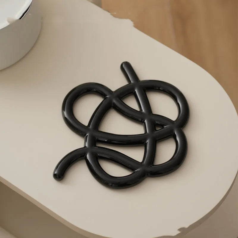 Modern irregular-shaped ceramic heat proof mat in grey on a wooden table protecting it from a hot pan.
