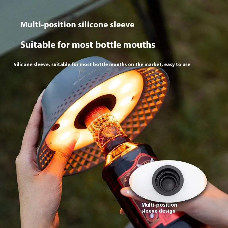 Beige wine bottle-shaped camping lantern with LED light on a wooden surface outdoors.