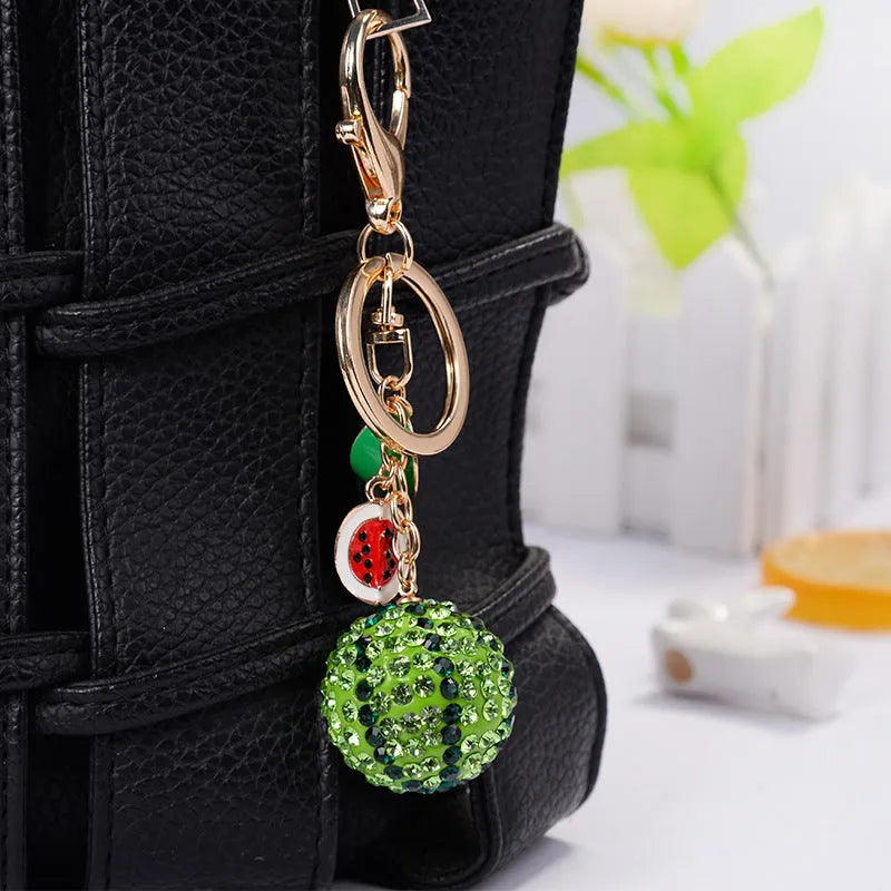 Green watermelon-shaped metal keychain on a white background.