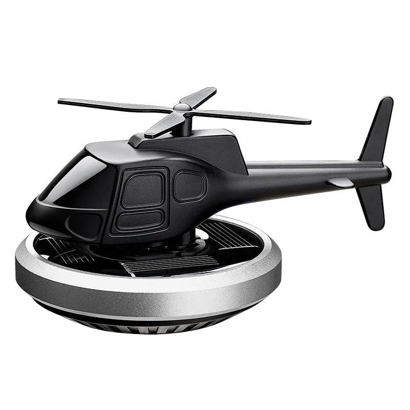 Silver metal solar-powered helicopter car air freshener with rotating blades on a dashboard