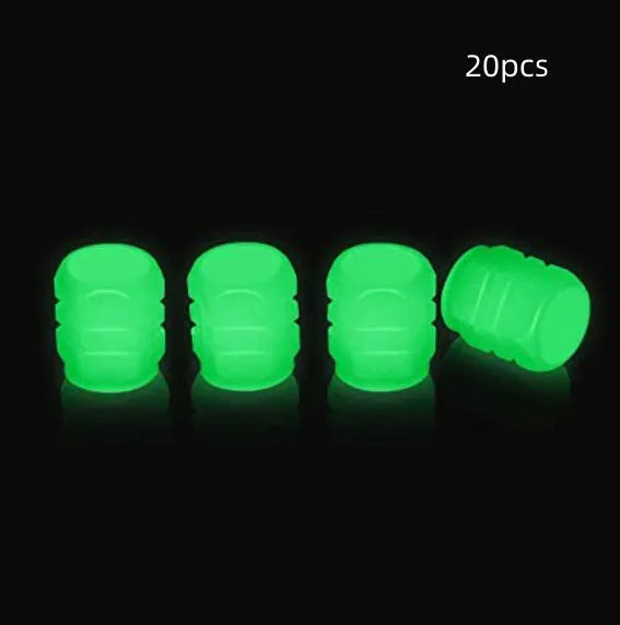 Set of four glowing green LED tyre valve caps screwed onto a car wheel valve stems at night.