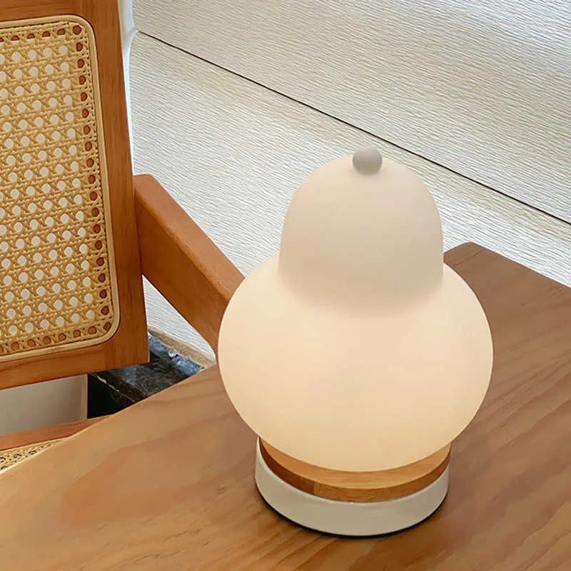 White pear-shaped rechargeable touch LED table lamp with PE shade on a wooden bedside table