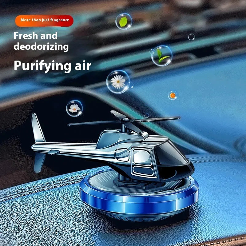 Silver metal solar-powered helicopter car air freshener with rotating blades on a dashboard