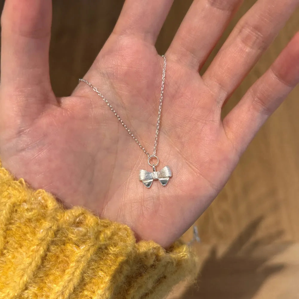 Matte bow pendant necklace in 925 silver with platinum electroplated finish on display