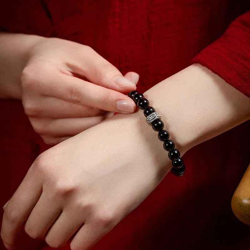 Obsidian bracelet with 8mm beads and a Tibetan zodiac charm on a wrist.