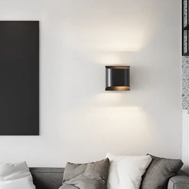 Minimalist copper wall lamp in black gold finish mounted beside a bed.