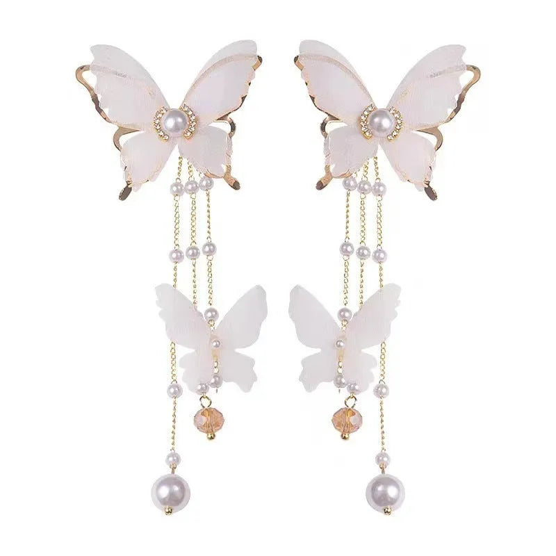 Close-up of white butterfly-shaped earrings with pearl and rhinestone details, featuring a dangling tassel on a model's ear.