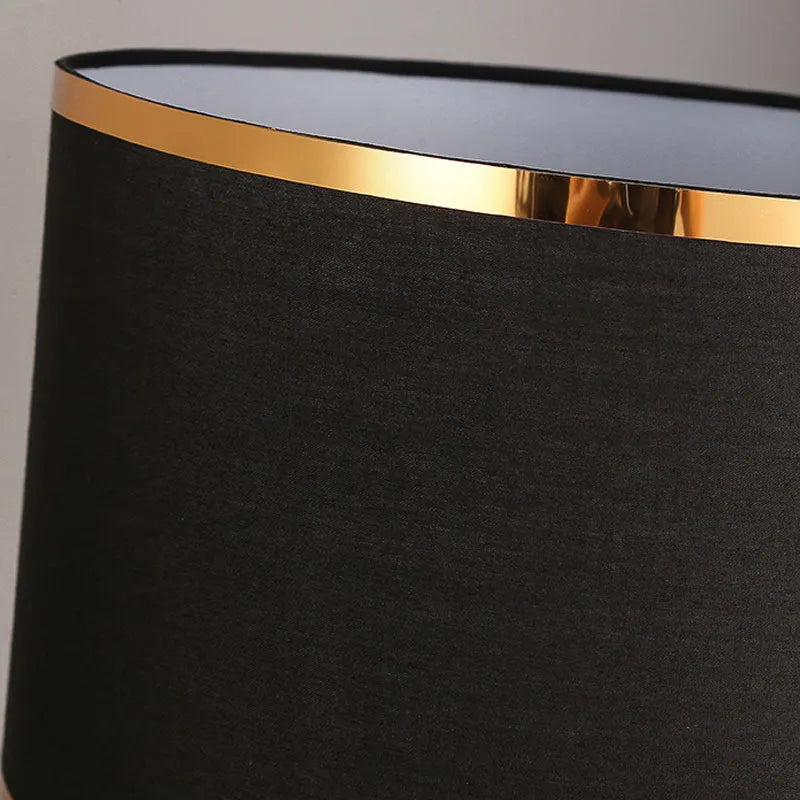 Iron table lamp with a white fabric shade and a push button switch on a wooden table.
