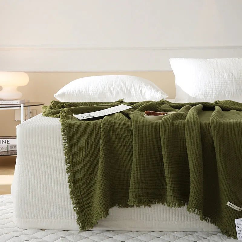 Cotton four-layer gauze blanket with tassel trim in avocado green colour, laid flat.