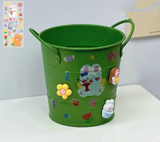 Round metal pen holder in a choice of colours, some with decorative sticker patches, on a wooden desk.