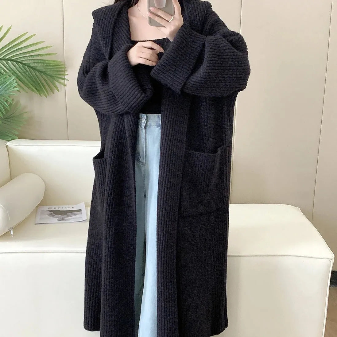 A woman wearing a long, loose, hooded cardigan coat in a neutral colour, showing its oversized fit and length.