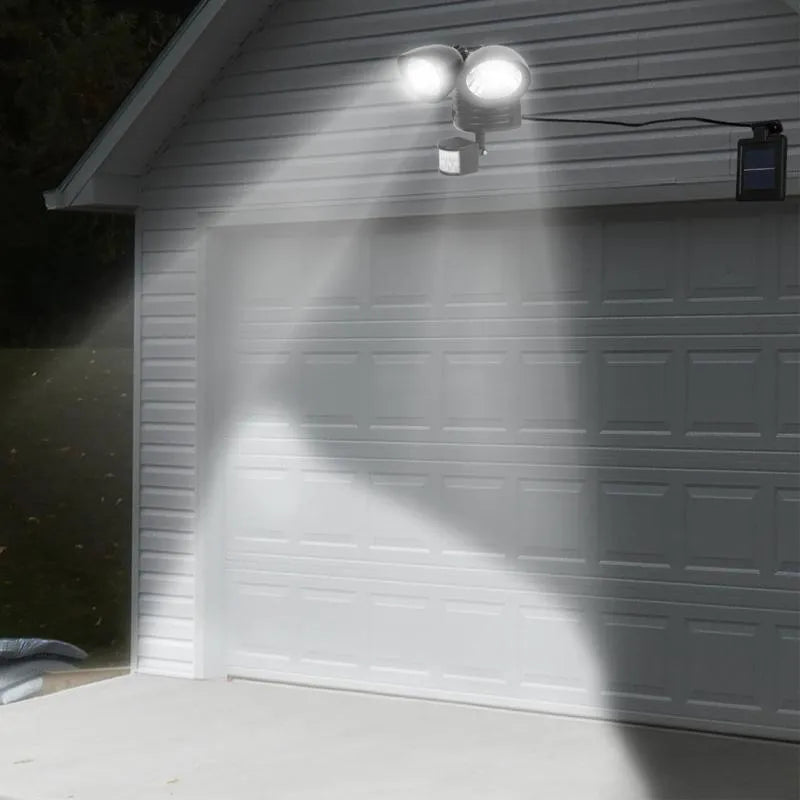 Black dual-head solar security spotlight with solar panel on top mounted on an outdoor wall.