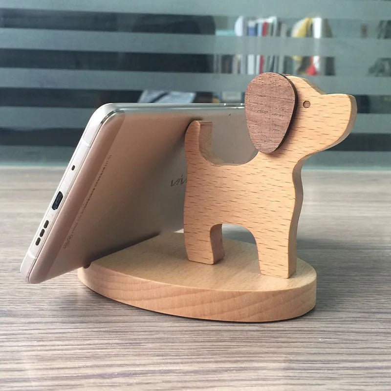 Solid beech wood phone stand with a decorative resin puppy figurine, holding a mobile phone at an angle with a charging cable threaded through the back.