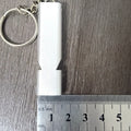 A silver or gold coloured aluminium alloy survival whistle with two holes on a grey background.