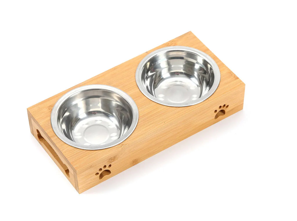 Solid wood elevated pet feeder with stainless steel bowls in a bamboo finish on a wooden floor.