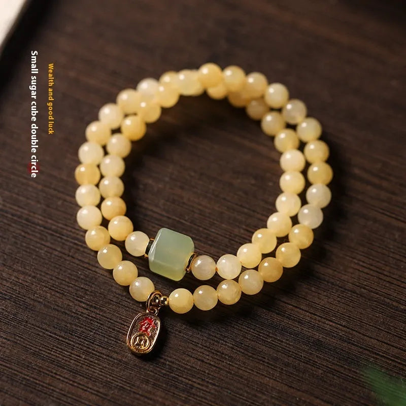 Close-up of a women's hand-woven bracelet with topaz-coloured barrel beads, square jade beads, and a fu charm.